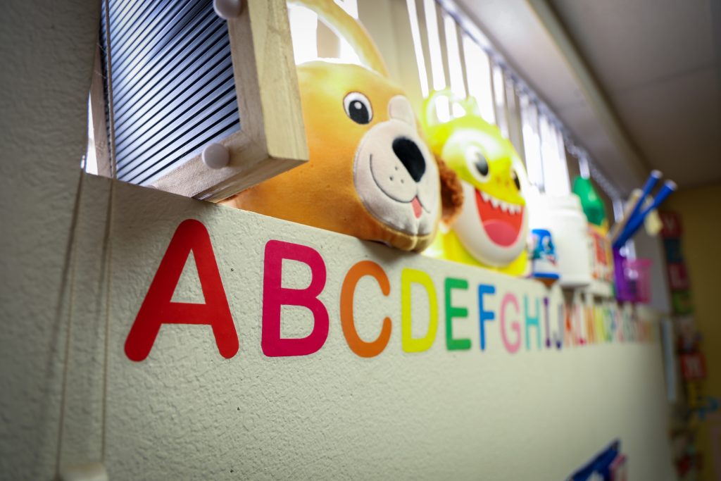 Picture of some toys on a window sill including a stuffed tiger head, a plastic bright yellow shark, and the letters of the alphabet on the well below